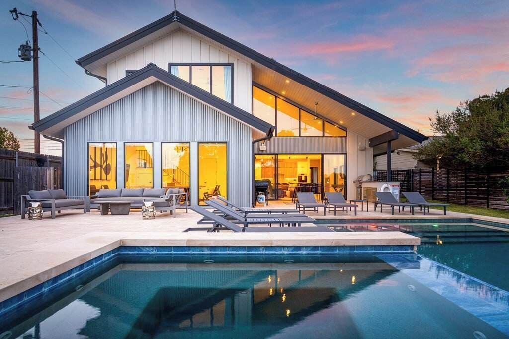 A modern two-story house with a swimming pool, outdoor seating, and a large glass door entrance.