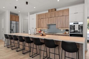 A modern kitchen with a central island, bar stools, wooden cabinets, and stainless steel appliances. - Kingsland Cove - Sleeps 20, Pool & Lake LBJ Dock (Kingsland)
