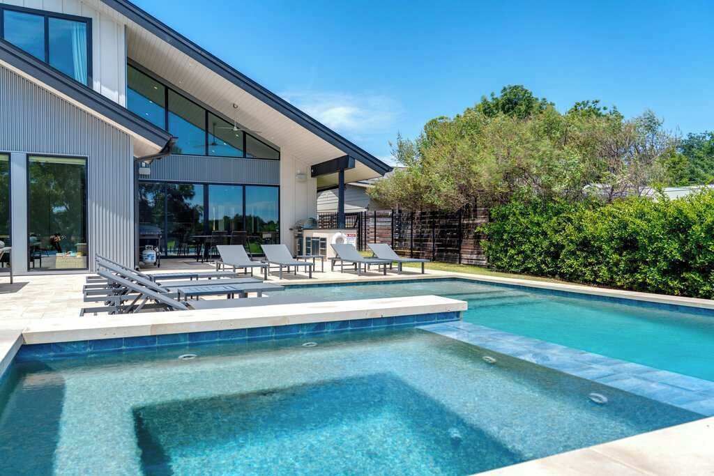 Een modern huis met een zwembad, lounge fauteuils en een overdekt terras.