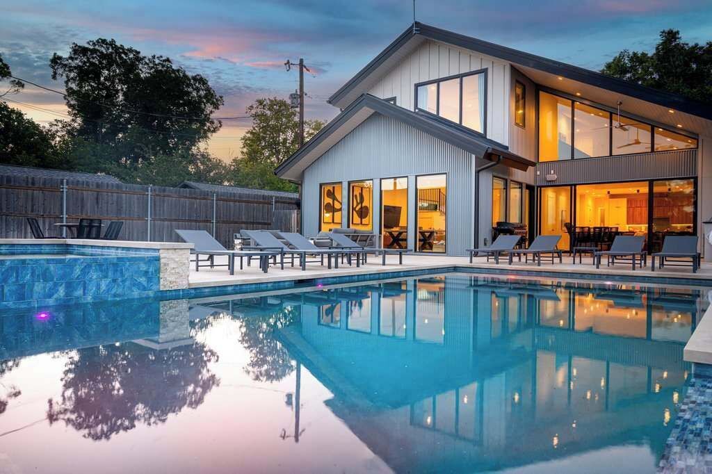 A modern house with a swimming pool, lounge chairs, and a large windowed room.