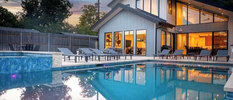 A modern house with a swimming pool, lounge chairs, and a large windowed room.