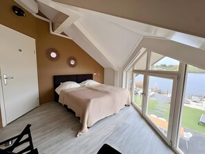 Ein Schlafzimmer mit einem Bett, einer Tür und einem großen Fenster mit Blick auf ein Gewässer.