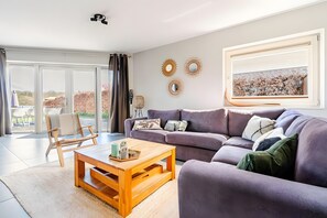 Un salon moderne avec un canapé, une table basse et une vue sur un jardin grâce à de grandes fenêtres.
