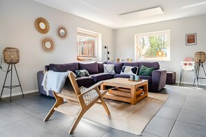 A modern living room with a sectional sofa, a coffee table, a woven chair, and decorative wall art. - Holiday Home 'Beachvilla with Sauna' with Lake View, Wi-Fi and Air Conditioning (Westerhaar-Vriezenveensewijk)