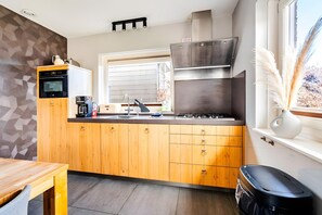 Eine moderne Küche mit Holzausstattung, einem eingebauten Backofen, einem Fenster mit Jalousien und einem Herd.