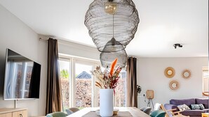 A modern dining area with a wooden table, chairs, a vase with flowers, and a hanging light fixture. - Holiday Home 'Beachvilla with Sauna' with Lake View, Wi-Fi and Air Conditioning (Westerhaar-Vriezenveensewijk)