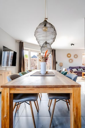 Un comedor moderno con una mesa de madera, sillas, un jarrón con flores y una lámpara colgante.