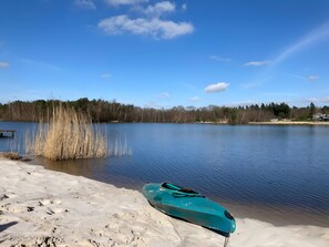 Ein ruhiger See mit einem Kajak am sandigen Ufer, umgeben von Bäumen und blauem Himmel.