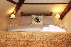 A bedroom with a checkered bedspread, a pillow with a bee design, two bedside lamps, and a wooden headboard. - Honey Bee Cottage (Liskeard)