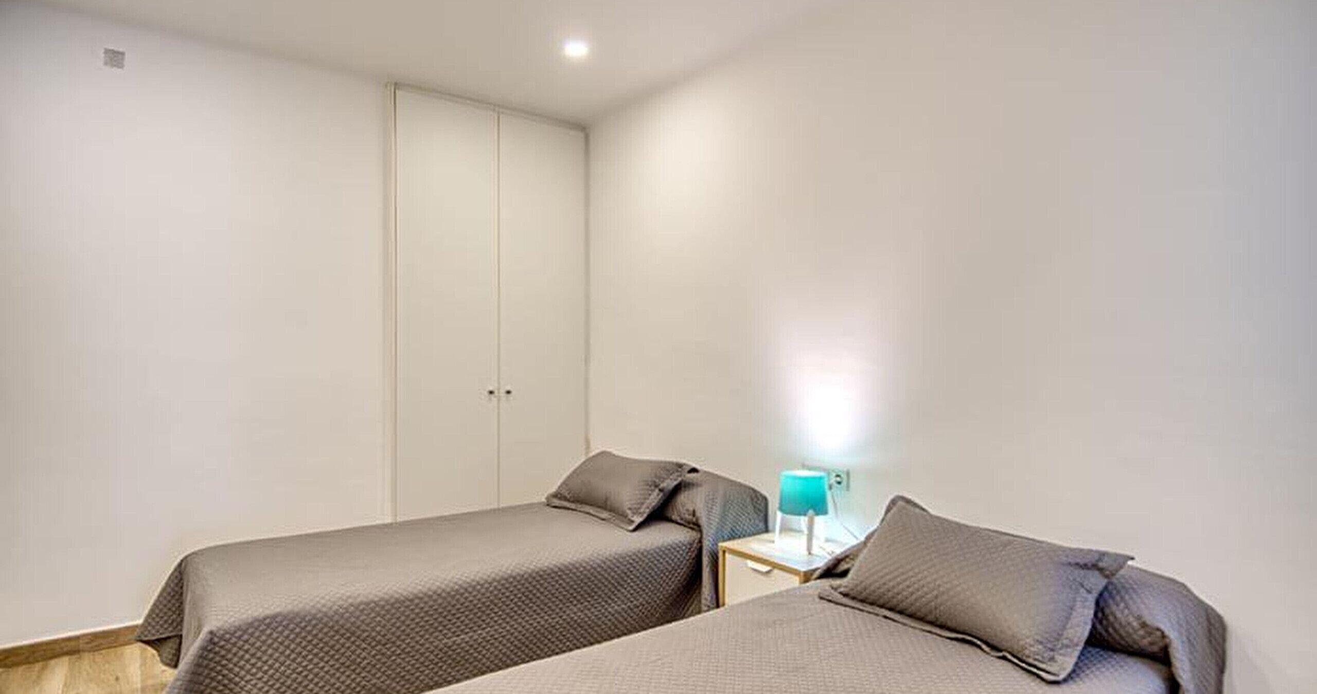 A bedroom with two single beds, a nightstand with a lamp, and a wardrobe.