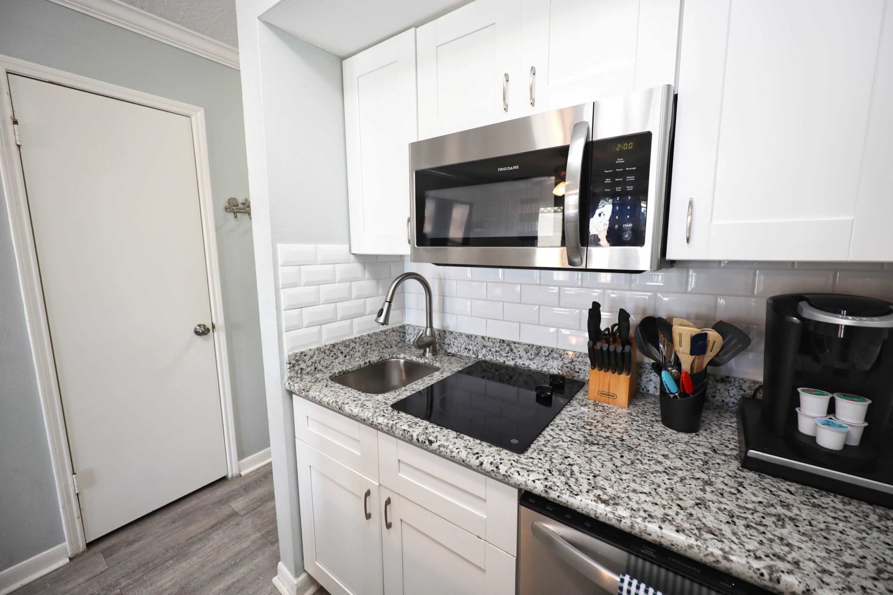 A modern kitchen with white cabinetry, a granite countertop, a stainless steel dishwasher, a coffee maker, and a microwave.