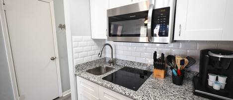 A modern kitchen with white cabinetry, a granite countertop, a stainless steel dishwasher, a coffee maker, and a microwave.