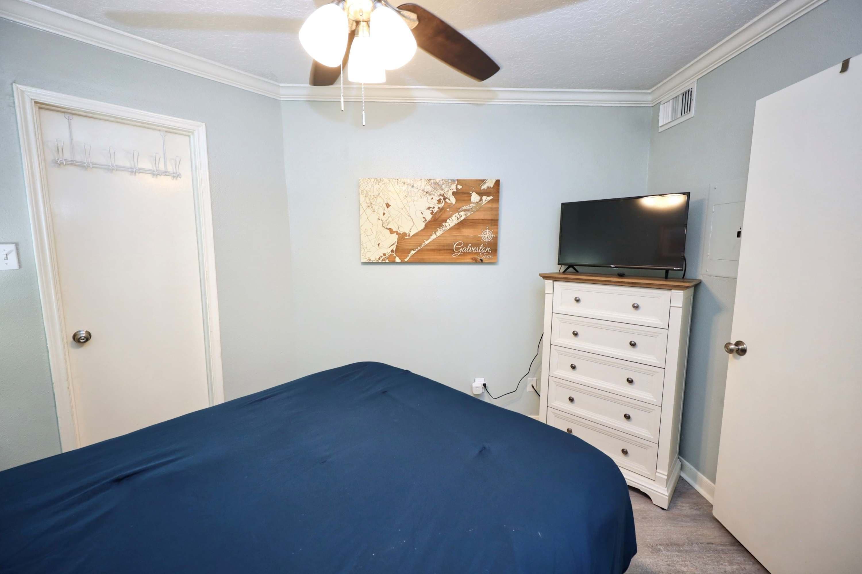 Une chambre à coucher comprenant un lit, une commode, un téléviseur et un ventilateur de plafond.