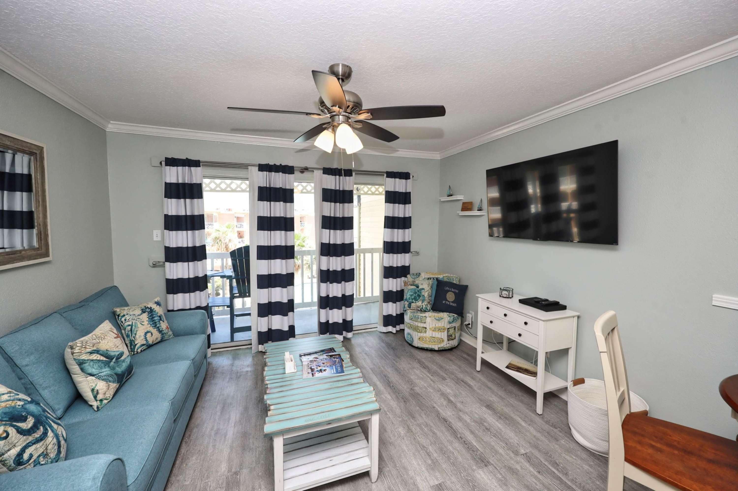 A living room with a sofa, a coffee table, a desk, and a ceiling fan.