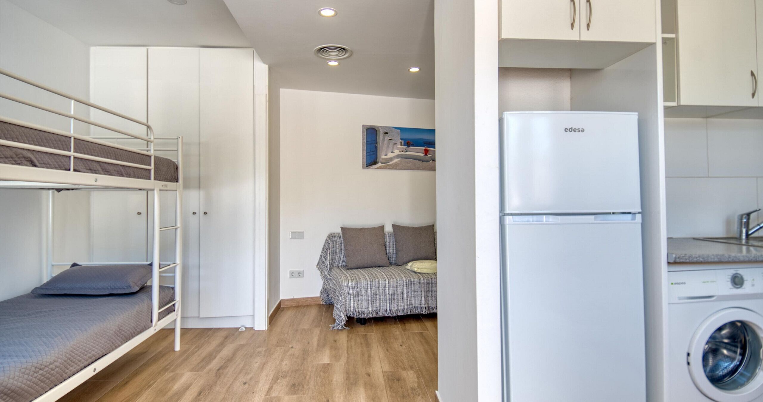 A compact room with a bunk bed, a sofa, a washing machine, and a small kitchen area.