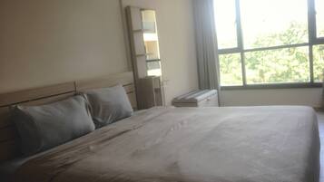 A hotel room with a large bed, a nightstand, a mirror, and a window with a view of trees.