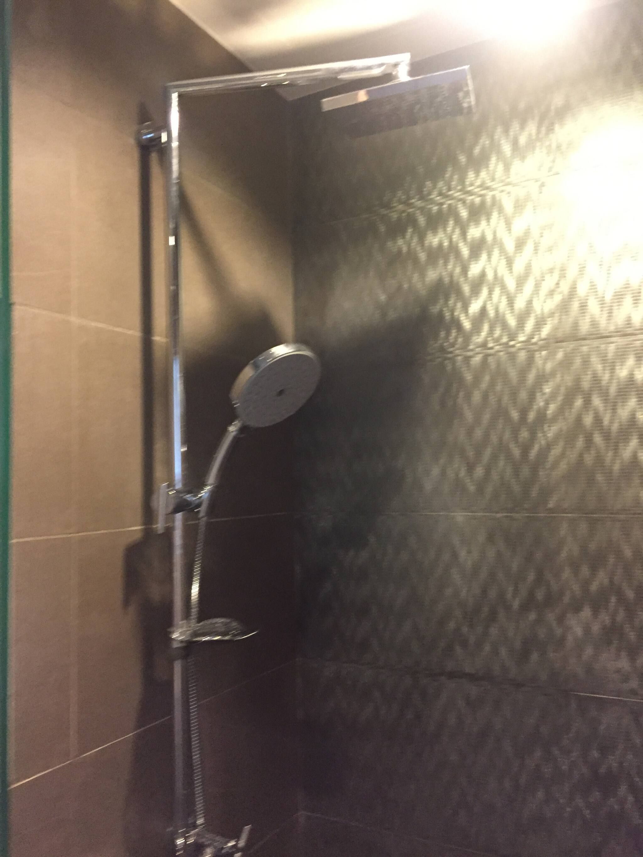 Ducha con cabezal de mano, panel de control en la pared y suelo de baldosas.