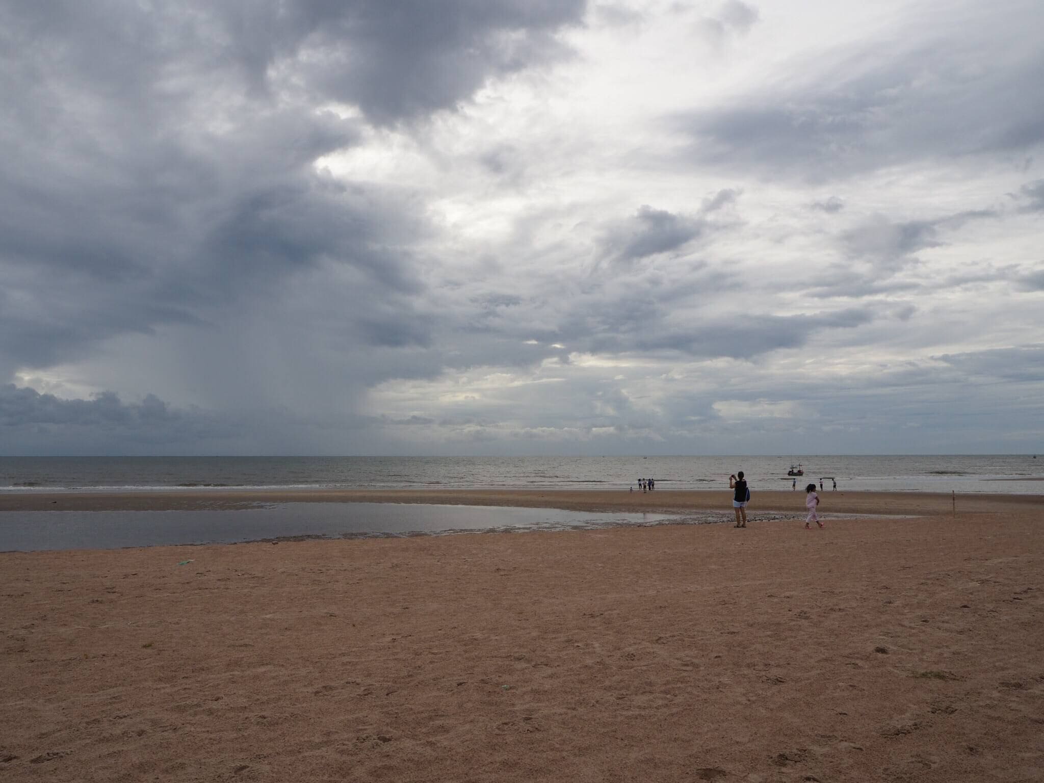 A beach with a wide sandy area and a calm sea under a cloudy sky.