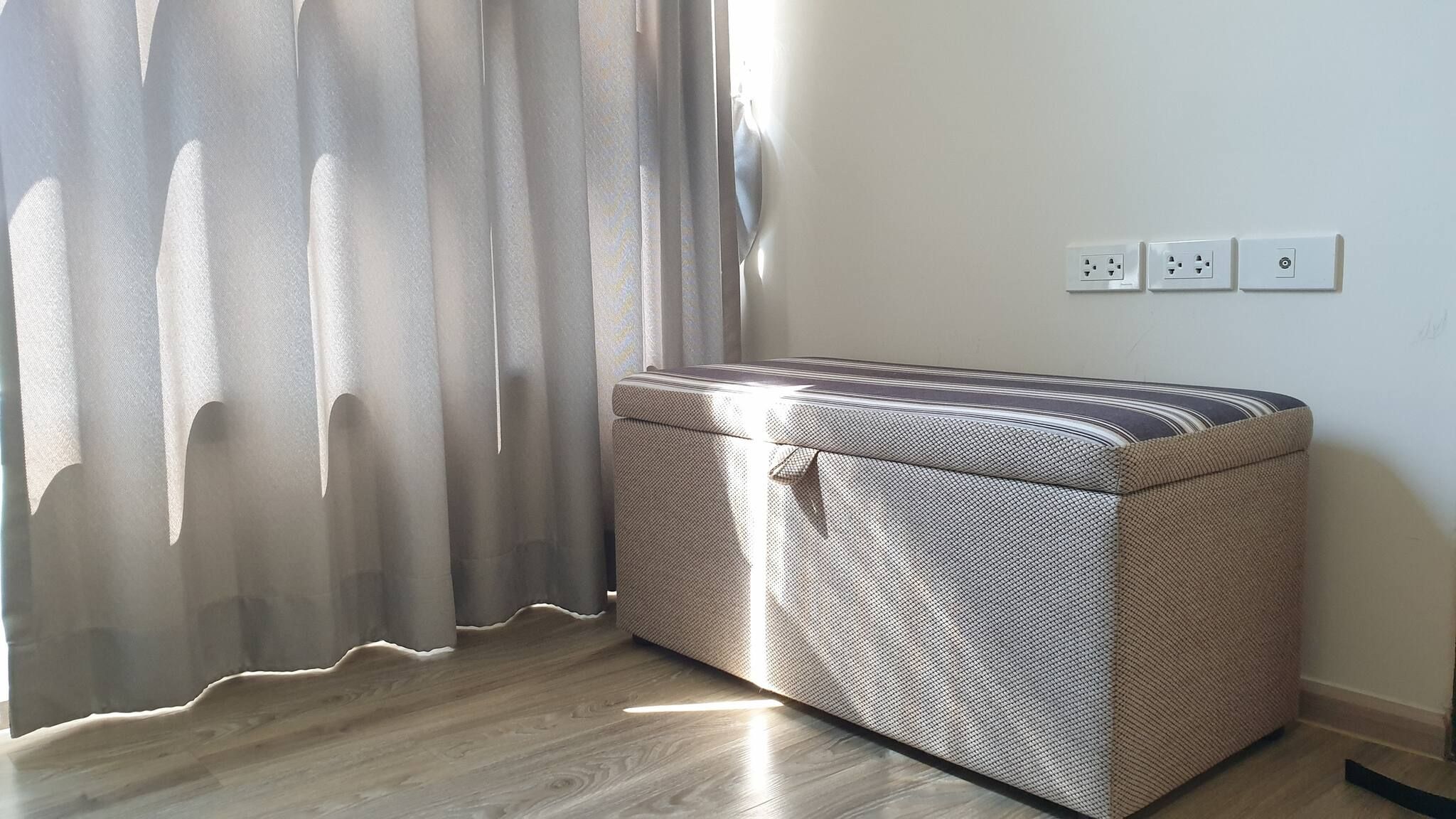 A room with a large, patterned storage unit against a wall, a window with sheer curtains, and a power outlet with three sockets.