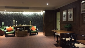 Una stanza con pavimento in mattoni, un divano verde con cuscini arancioni, un tavolo di legno e un muro con decorazione testurizzata.