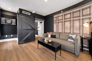 A modern living room with a sofa, coffee table, and a dartboard. - The Penn Hotel - Party in Gaslamp! Chic 2BR for 6! (San Diego)