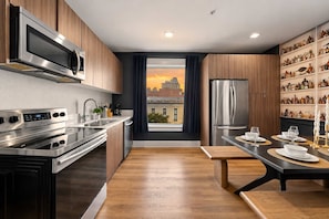 Een moderne keuken met roestvrijstalen apparatuur, een eethoek met uitzicht op een stadsbeeld en een plank met diverse keukenspullen.