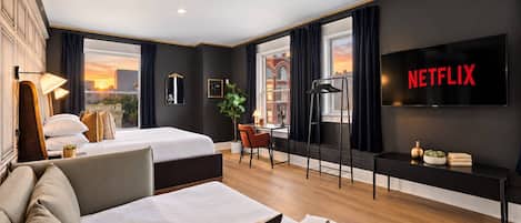 Habitación de hotel con cama, sofá, escritorio, televisor y vistas a la ciudad.