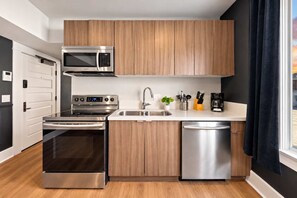 A modern kitchen with stainless steel appliances, wooden cabinets, a sink, and a window with curtains. - The Penn Hotel - Party in Gaslamp! Chic 2BR for 6! (San Diego)