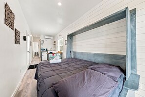 A bedroom with a large bed, a kitchenette, and a bathroom. - Container Retreat: Unit 13 (Fredericksburg)
