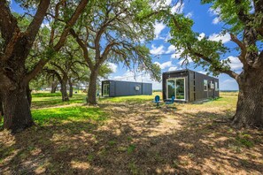 A modern, metal-framed building with large windows, surrounded by mature trees and a grassy field. - Container Retreat: Unit 13 (Fredericksburg)