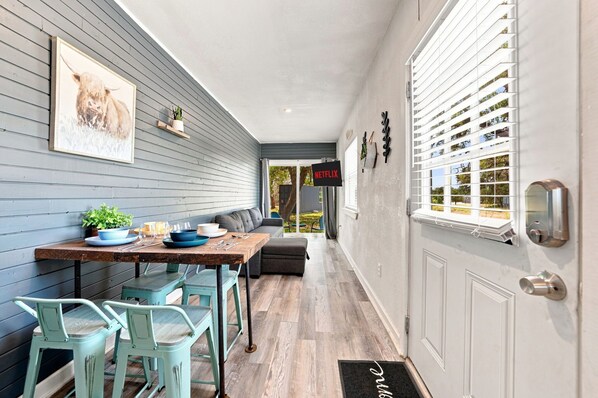 A dining area with a table set for four, a bench, and a door with a doormat.