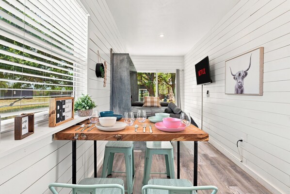 A modern dining area with a wooden table, teal chairs, and a TV mounted on the wall.