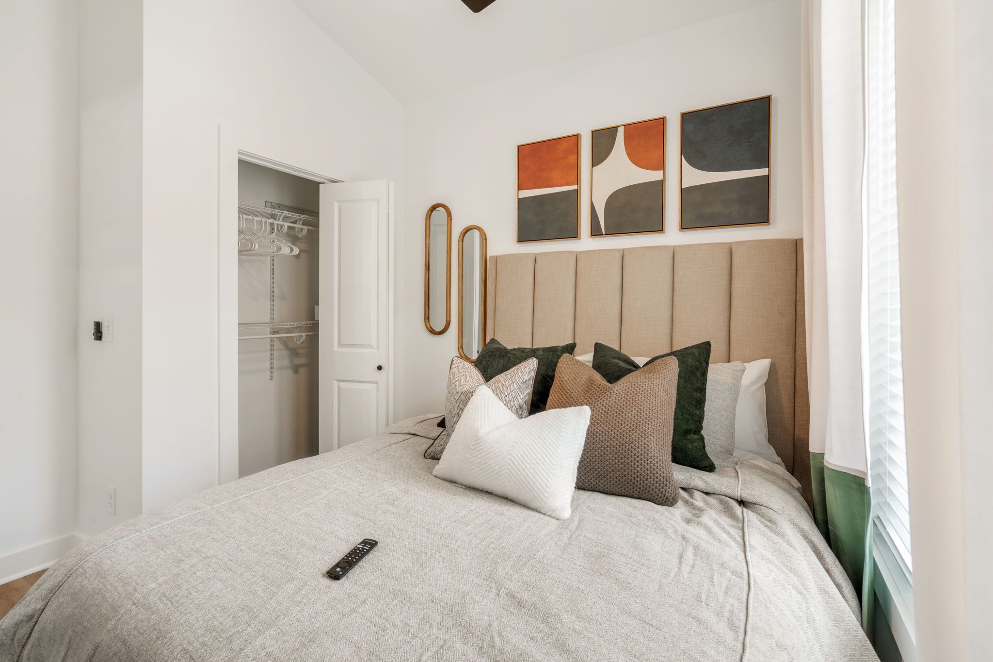 A bedroom with a bed, pillows, a remote control, a wardrobe, and artwork on the wall.