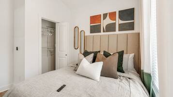 A bedroom with a bed, pillows, a remote control, a wardrobe, and artwork on the wall.