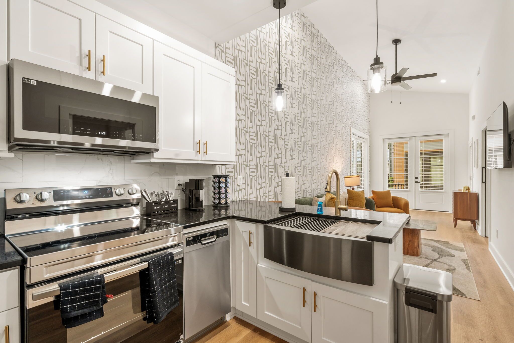 A modern kitchen with stainless steel appliances, white cabinetry, and a patterned backsplash.