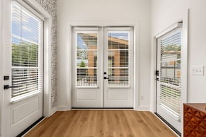Puertas dobles con un diseño geométrico en la pared, piso de madera y vista a un edificio a través de las puertas.
