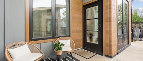 A modern building exterior with a large window, a door with a security camera, and a small table with chairs.