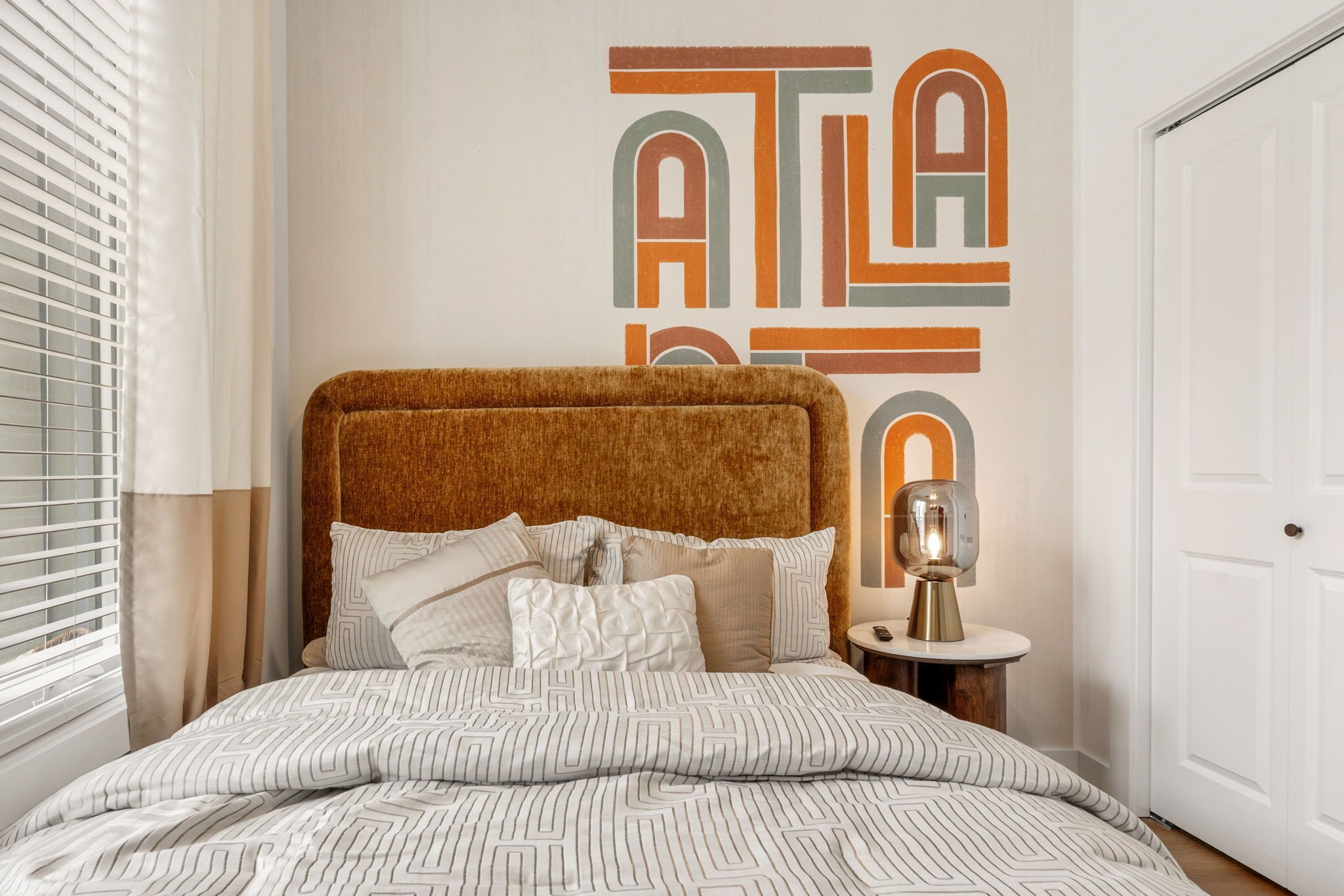 Un dormitorio con una cama grande, una mesita de noche con lámpara y una pared decorada con arte abstracto.
