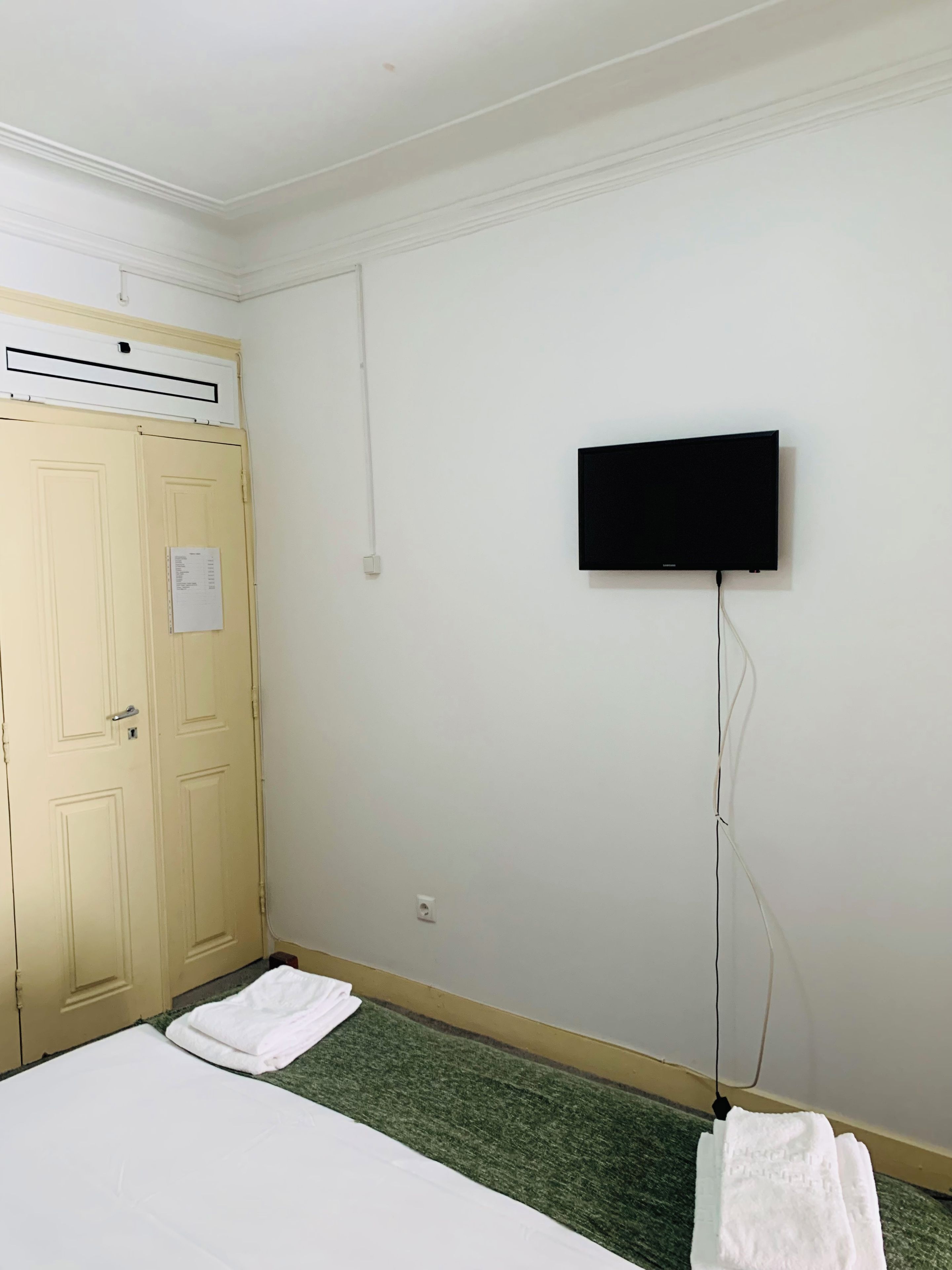 A room with a bed, a television mounted on the wall, and a door with a paper on it.