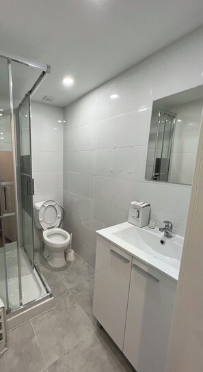 A modern bathroom with a toilet, sink, and shower area. - São Lázaro Bhuiyan Family Host (Lisbon)