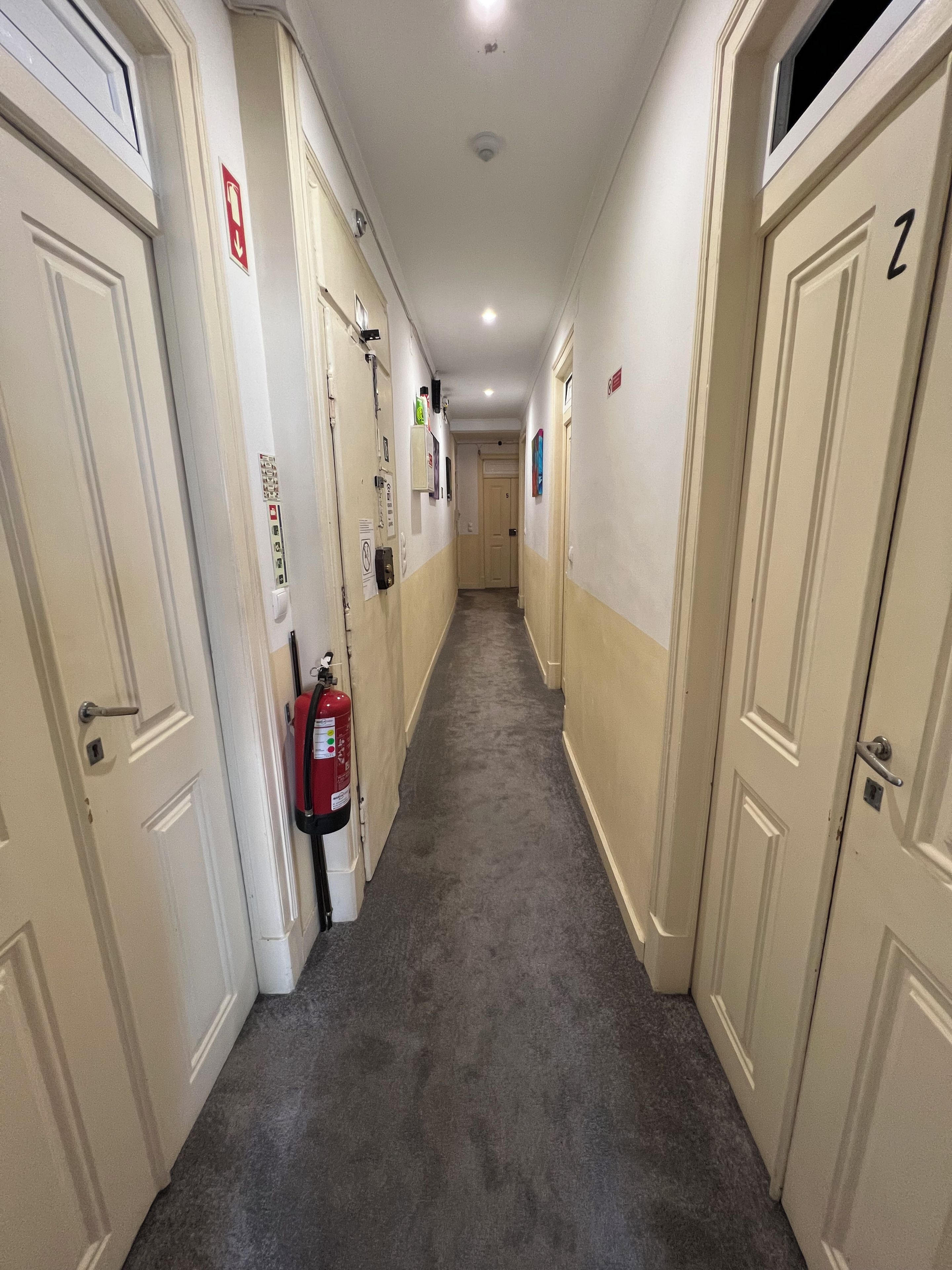 A corridor with doors on both sides, a fire extinguisher mounted on the wall, and a ceiling light.