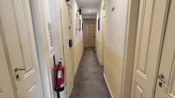 A corridor with doors on both sides, a fire extinguisher mounted on the wall, and a ceiling light.
