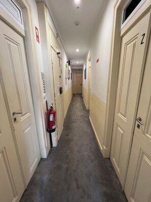 A corridor with doors on both sides, a fire extinguisher mounted on the wall, and a ceiling light. - São Lázaro Bhuiyan Family Host (Lisbon)