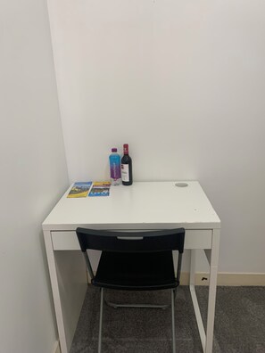 A white desk with a black chair, a bottle of wine, a water bottle, and a few books. - São Lázaro Bhuiyan Family Host (Lisbon)
