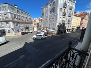 A street view with buildings, parked cars, and a clear sky. - São Lázaro Bhuiyan Family Host (Lisbon)
