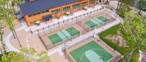 Un immeuble à plusieurs étages doté d’un terrain de sport, d’un espace extérieur aménagé pour s’asseoir et d’un parking.