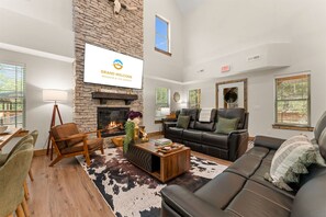 Un amplio salón con chimenea de piedra, sofás de cuero, una mesa de centro y una gran pantalla de televisión mostrando 'GRAND WELCOME BRANSON & THE OZARKS'.