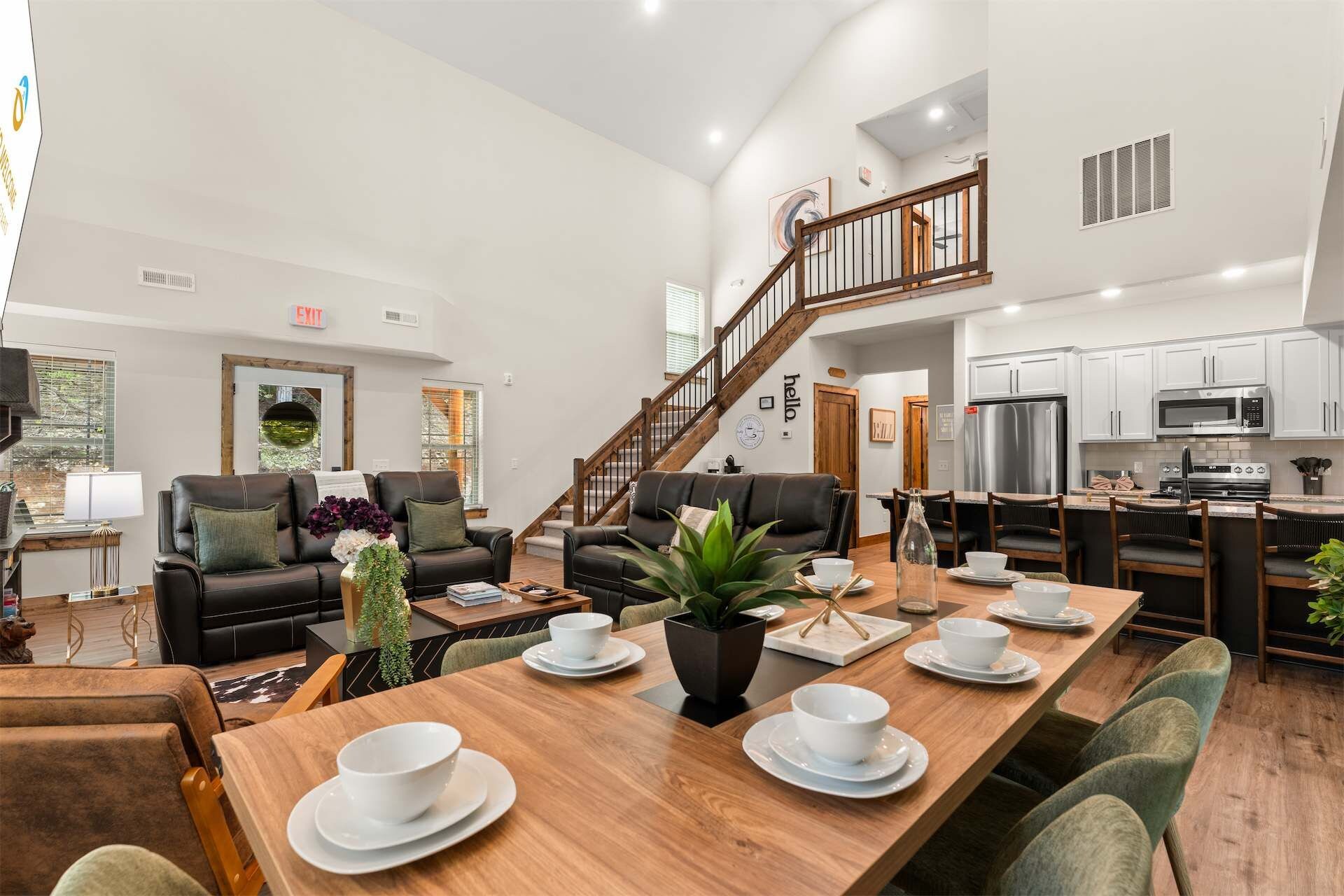 A spacious living area with a dining table set for four, a staircase leading to an upper level, and a modern kitchen with stainless steel appliances.