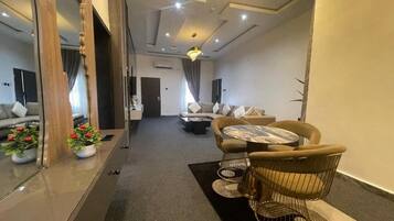A modern hotel room with a sofa, a round table, and a chair. There is a mirror on the left side and a door leading to another room.
