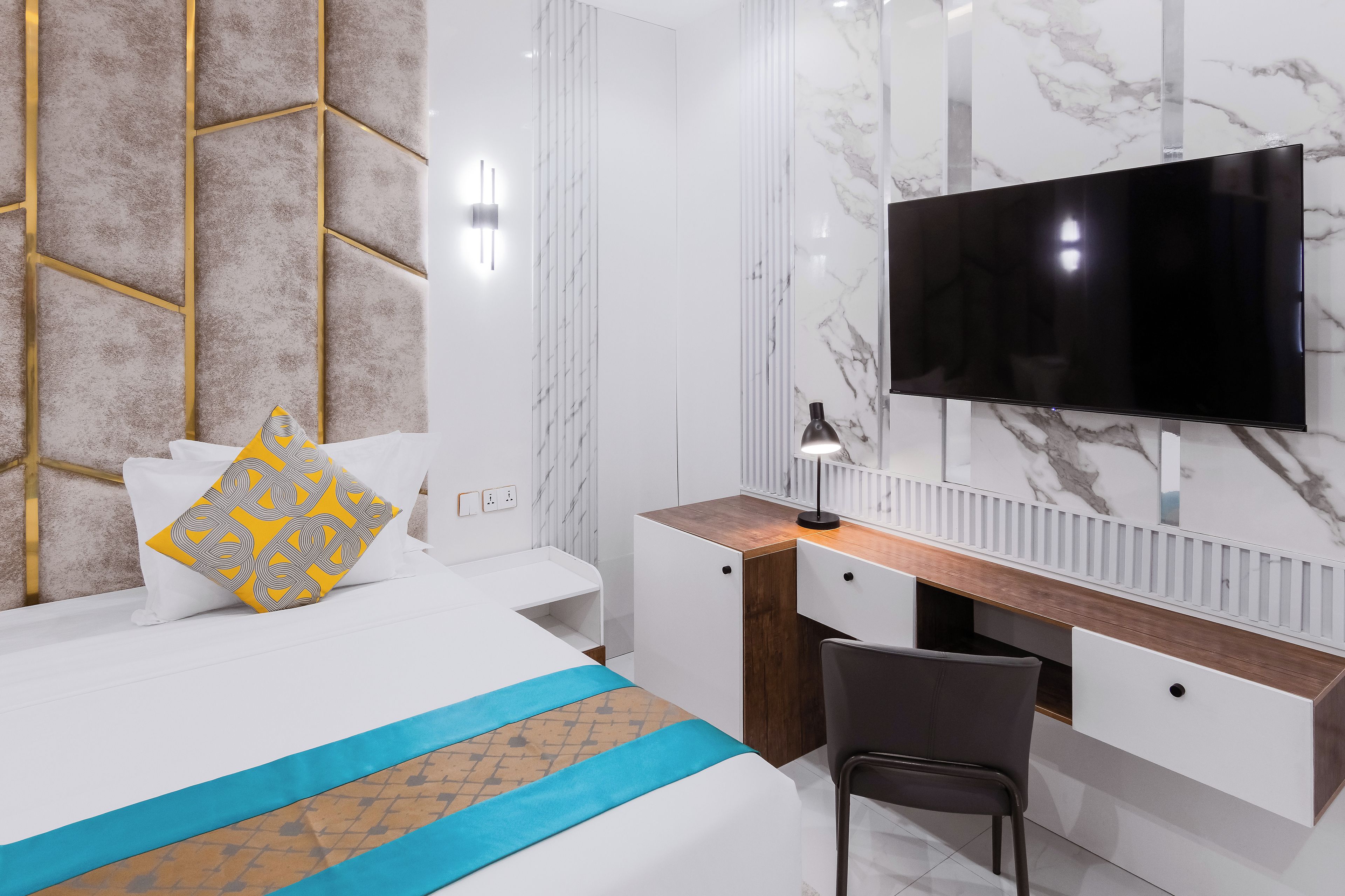 A modern hotel room with a bed, a desk, a chair, a television, and a marble wall.